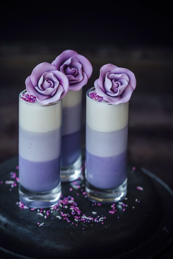 two glasses filled with purple flowers on top of a black plate and sprinkles