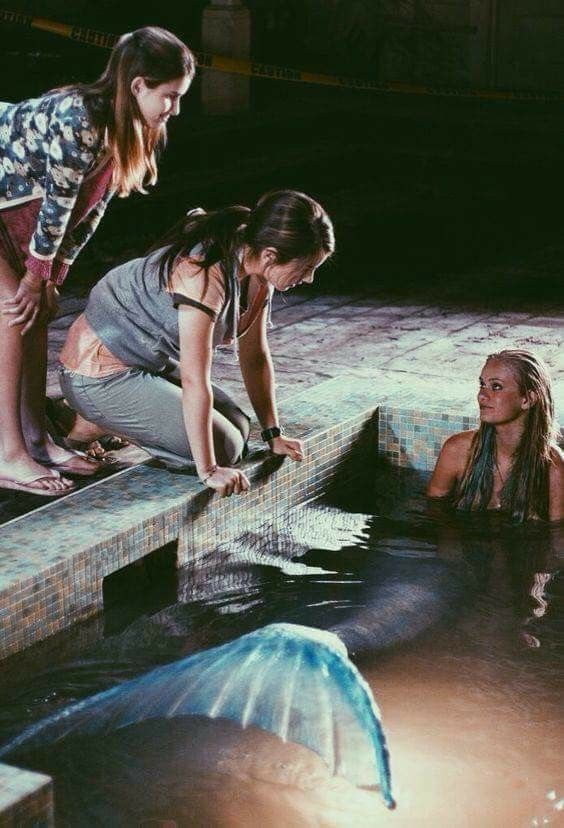 two girls are playing in the water with an umbrella while another girl looks at them