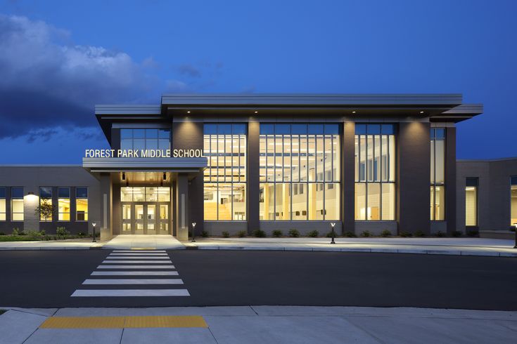 an empty parking lot in front of a large school building at night with the lights on