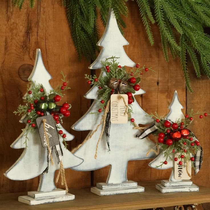 three white christmas trees with red berries and greenery on them are sitting on a shelf in front of a wood paneled wall