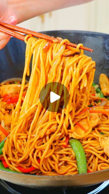 someone is holding chopsticks over noodles in a skillet with vegetables and sauce