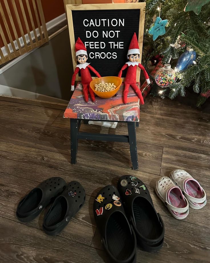 two elfs are sitting on a chair next to some shoes and a sign that says caution do not feed the crocs