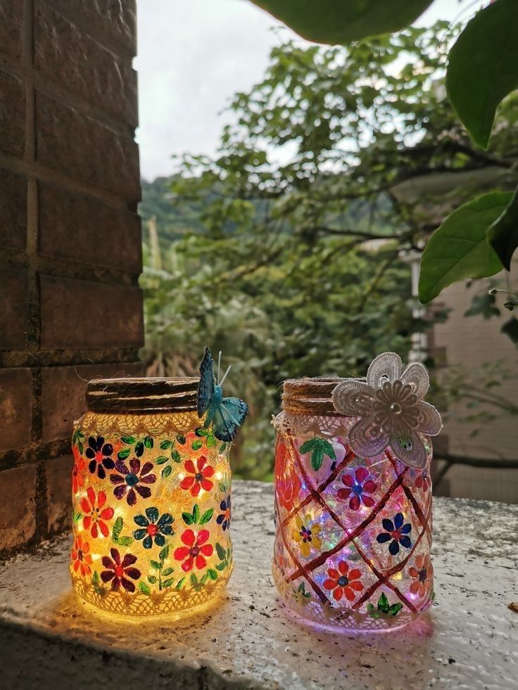 two colorful glass jars sitting next to each other on top of a stone wall with trees in the background