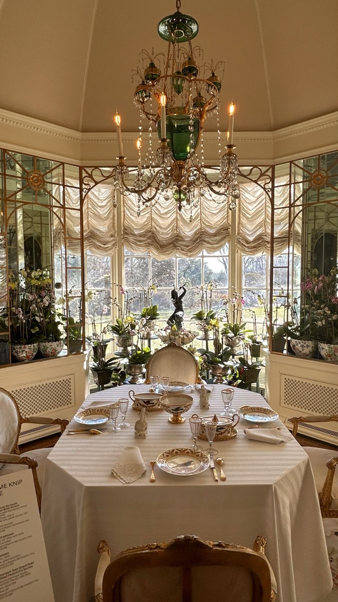 a dining room table set up with place settings and flowers in front of the window