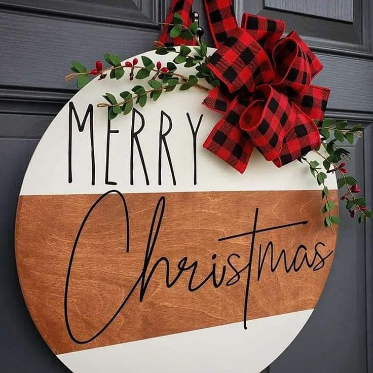 a merry christmas sign hanging on a door with red and black plaid bow around it