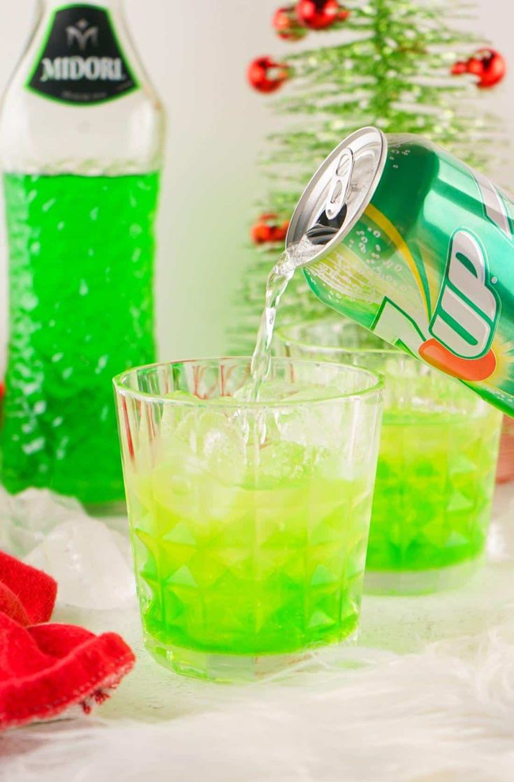 two glasses filled with green liquid next to a bottle of soda and a christmas tree