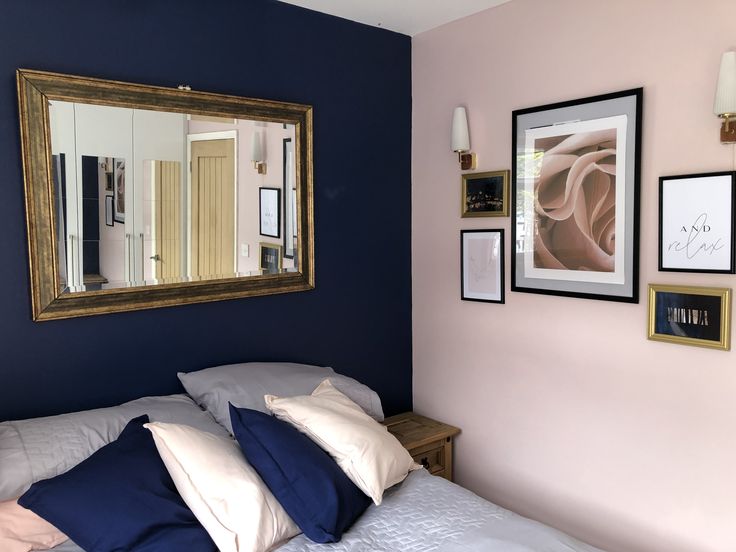 a bedroom with blue walls and white bedding, framed pictures on the wall above it