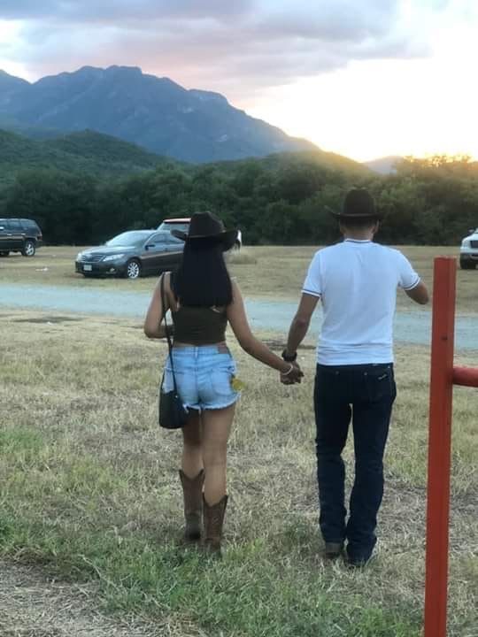 a man and woman holding hands while walking through a field with cars in the background