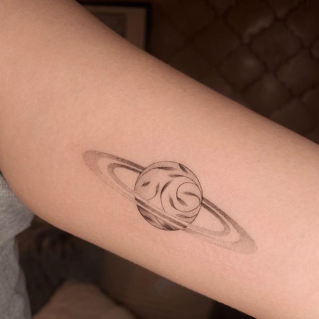 a small saturn tattoo on the arm