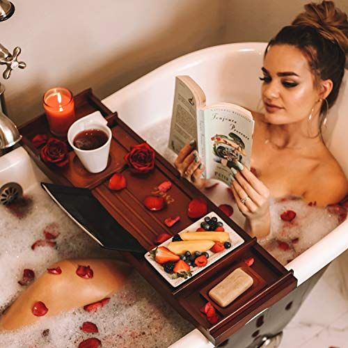 a woman sitting in a bathtub reading a book next to a bowl of fruit