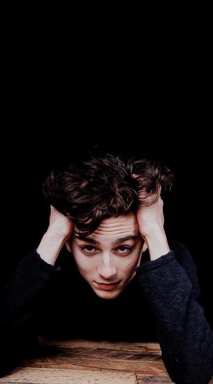 a young man sitting at a table with his hands on his head and looking down