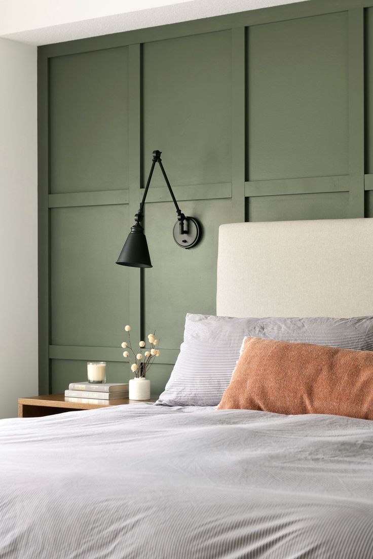 a bedroom with green paneled walls and a white bed topped with two orange pillows