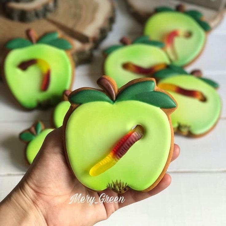 a hand is holding some decorated cookies in the shape of apples