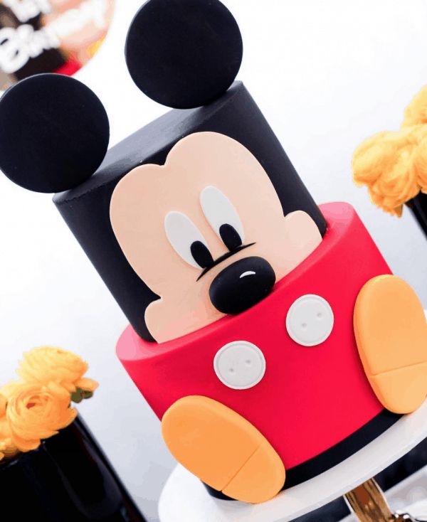 a mickey mouse cake with yellow flowers in the background