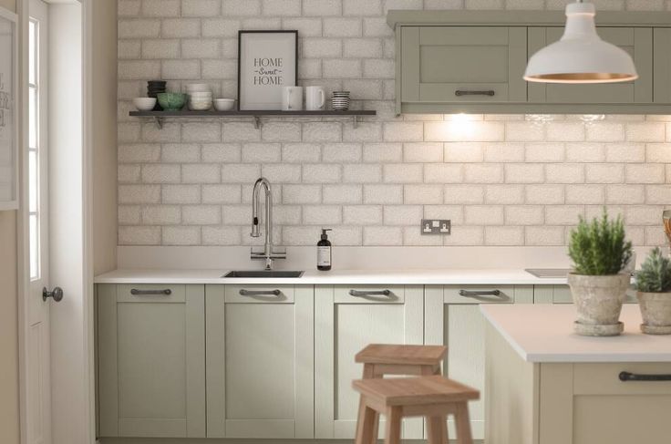 a white brick wall in a kitchen with wooden stools and green cabinetry next to the sink