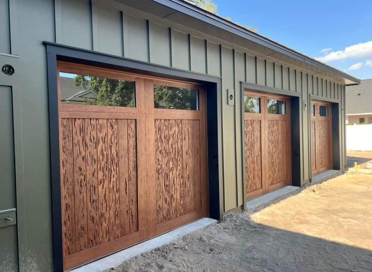 two wooden garage doors in front of a green building with brown trim on the side