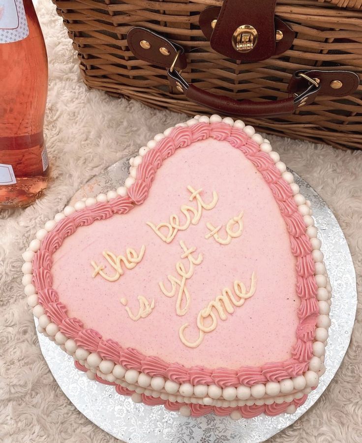 a heart shaped cake sitting on top of a table next to a basket and bottle