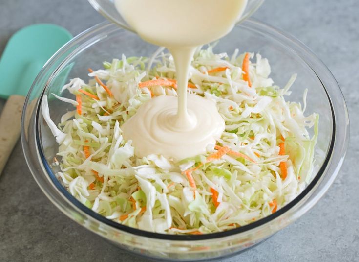 a bowl filled with coleslaw, carrots and mayonnaise being drizzled on top