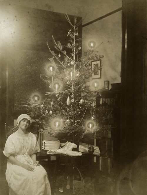 an old photo of a woman sitting in front of a christmas tree with lights on it