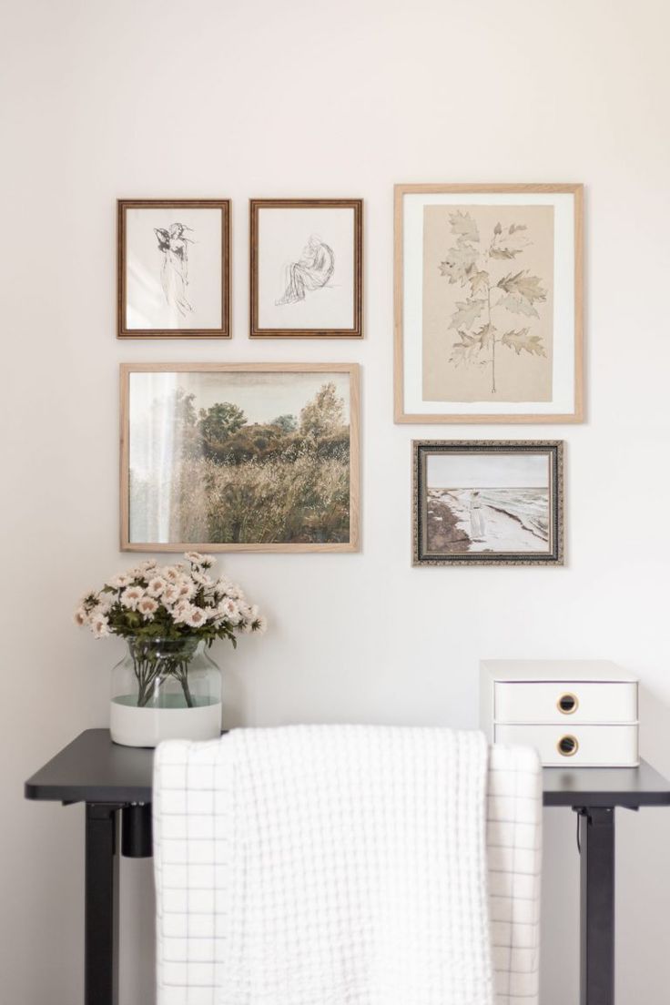 a white chair sitting under pictures on the wall next to a vase filled with flowers