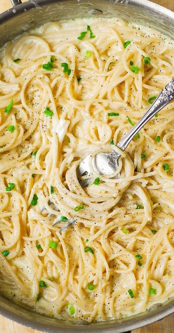 a pan filled with pasta and peas on top of a wooden table next to a silver spoon