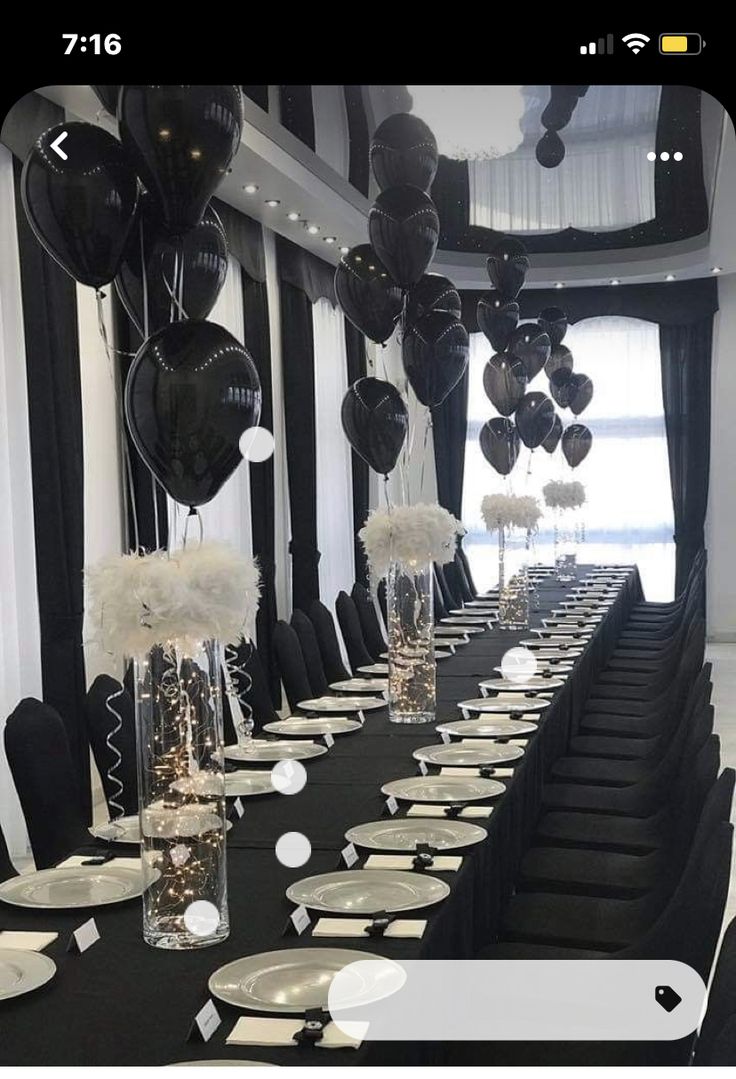 a long table is set up with black and white balloons, silverware, and place settings