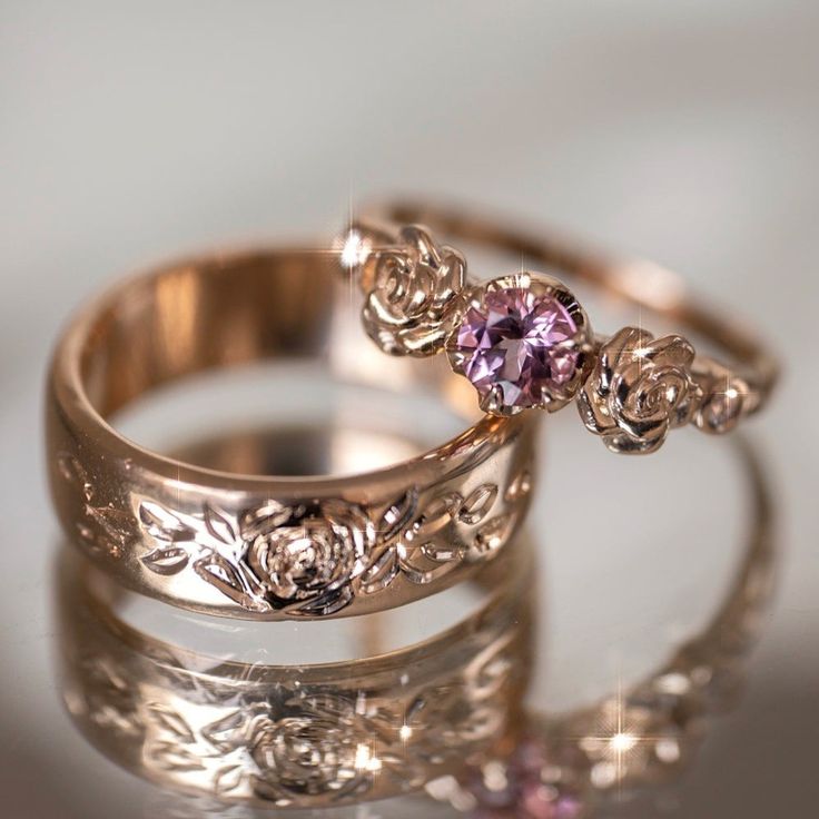 two gold wedding rings with an amethorate stone in the middle and floral designs on each band