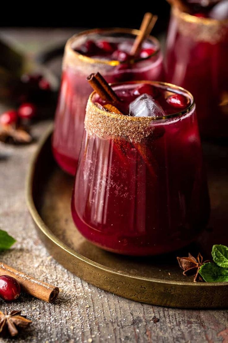 two glasses filled with cranberry punch on top of a wooden table next to cinnamon sticks