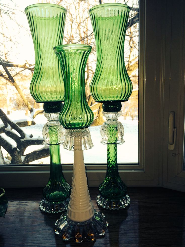 three green glass vases sitting on top of a wooden table next to a window