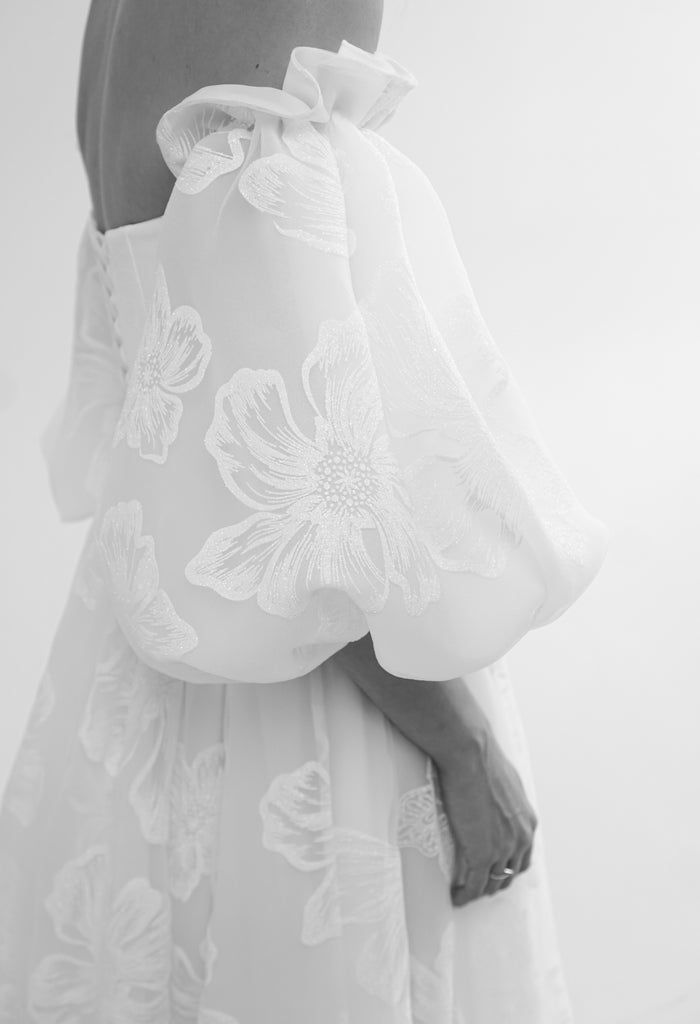 the back of a woman's dress with white flowers on it and her hand in her pocket