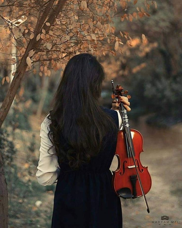 a woman with long black hair holding a violin in her right hand and looking down at the ground