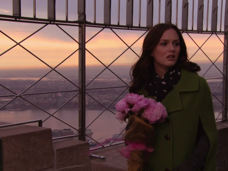 a woman standing on top of a tall building with a pink flower in her hand