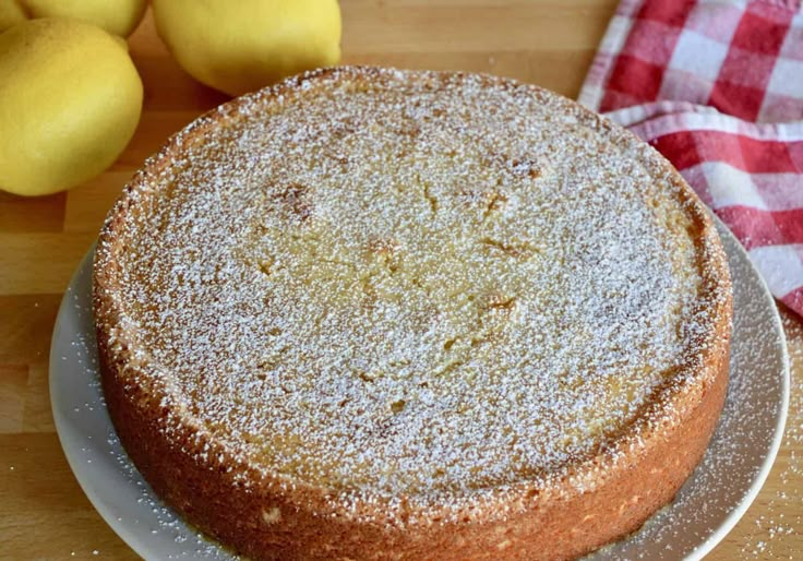 a cake sitting on top of a white plate covered in powdered sugar next to lemons