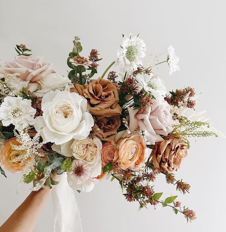 a bouquet of flowers is being held up by someone's hand in front of a white wall