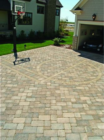 a brick driveway with a basketball hoop in the middle and two garages behind it