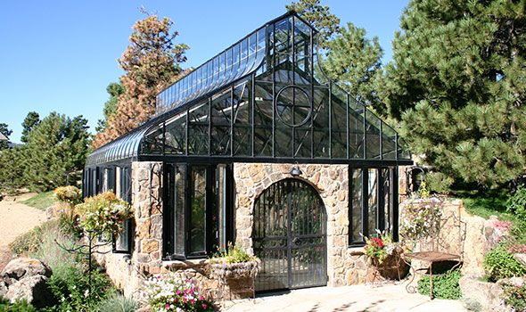 a building made out of rocks and glass with plants growing on the outside, surrounded by greenery