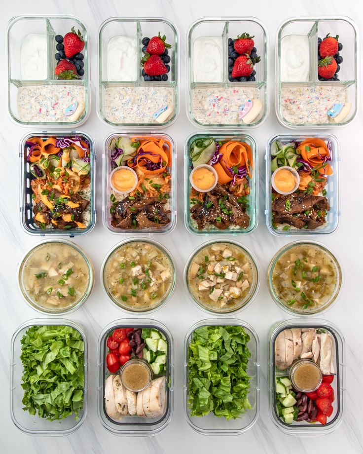 several containers filled with different types of food on top of a white countertop next to strawberries, carrots, celery, broccoli and other vegetables