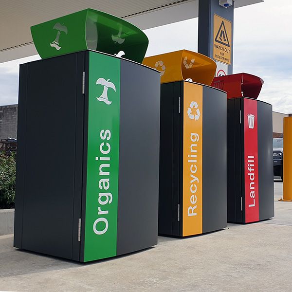 four different colored trash bins in front of a gas station with the word organic on them