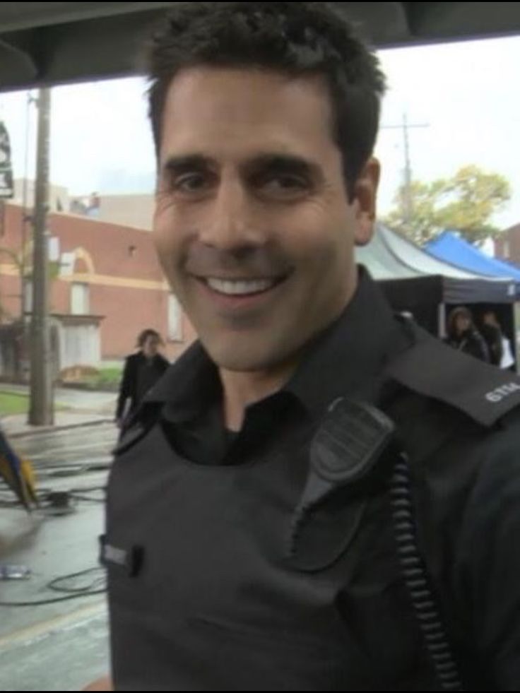 a police officer smiling for the camera in front of some people on a city street