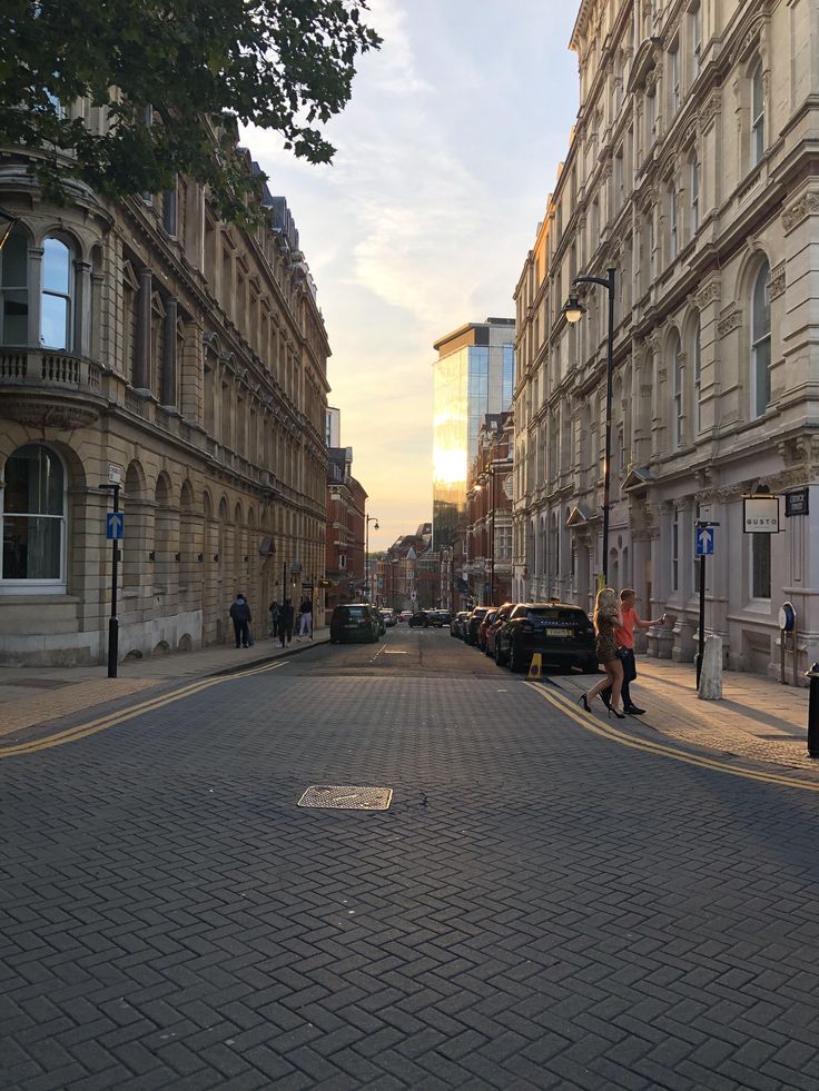 people are walking down the street in front of some tall buildings at sunset or dawn