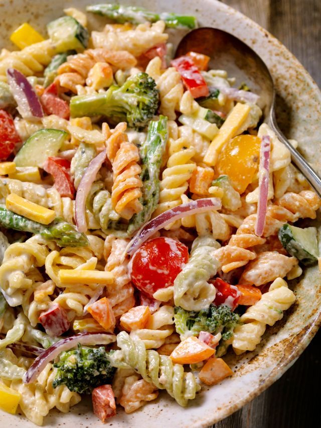 a pasta salad with tomatoes, broccoli, and onions in a wooden bowl