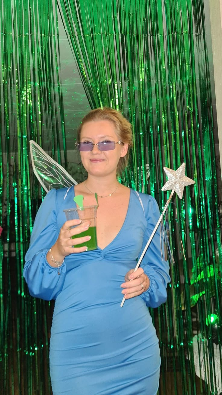 a woman in a blue dress holding a star wand and a green bottle with liquid