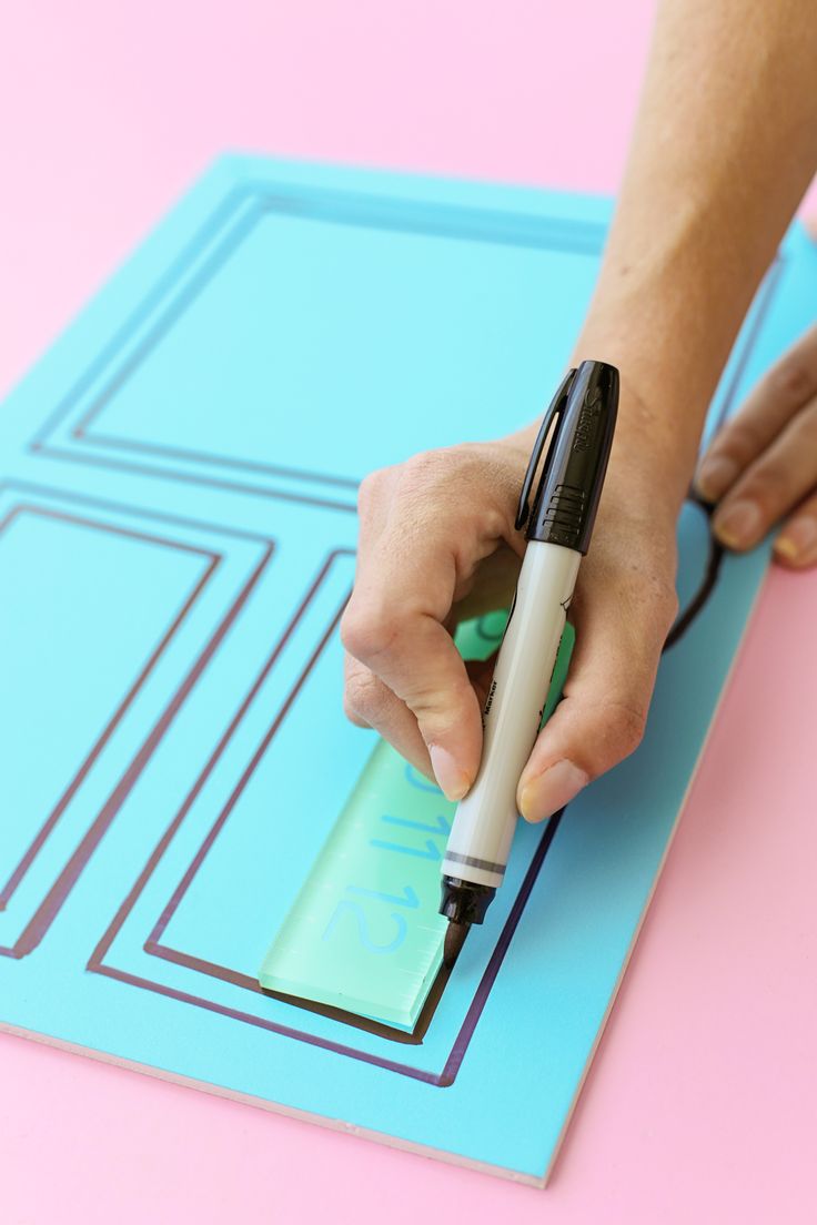 a person using a marker to draw on a piece of paper with a blue background