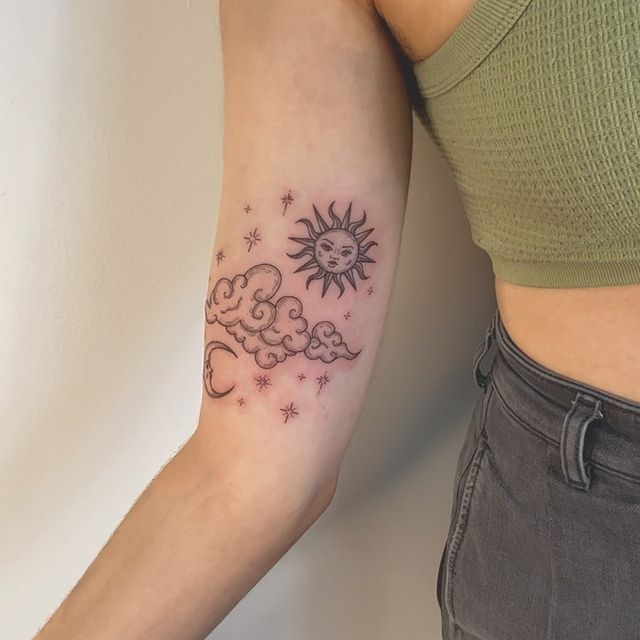 a woman with a sun and clouds tattoo on her arm, next to a wall