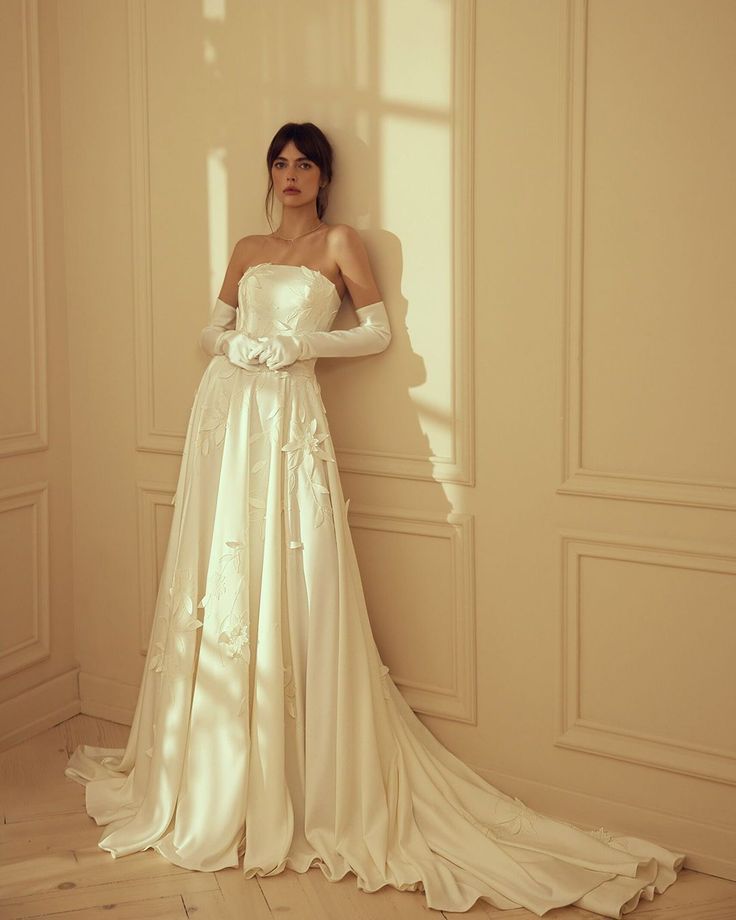 a woman in a wedding dress leaning against a wall with her hands on her hips