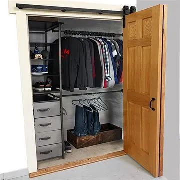 an open closet with clothes hanging on the wall and drawers below it, in front of a door