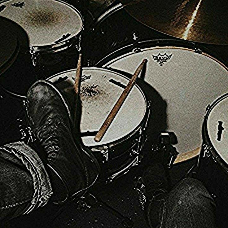 a person sitting in front of drums with their feet on the drum sticks and legs crossed