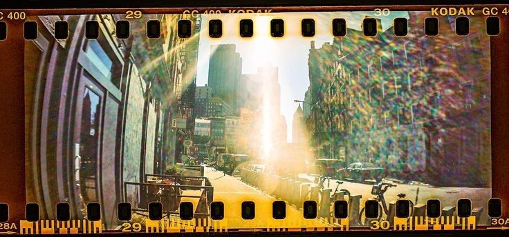 a film strip with an image of the sun shining through buildings and cars on it