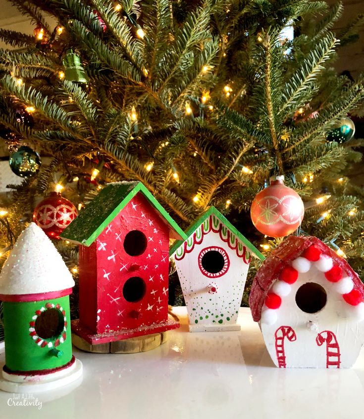 three colorful bird houses sitting next to a christmas tree