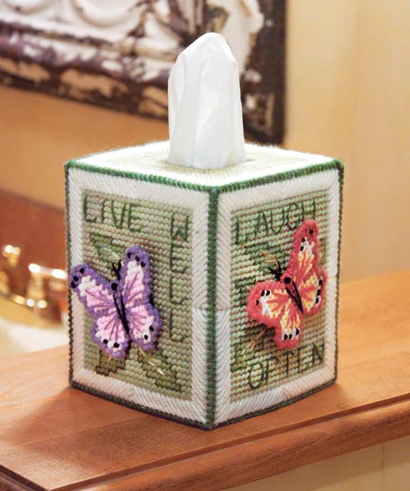 a tissue box with two butterflies on it sitting on top of a wooden table next to a mirror